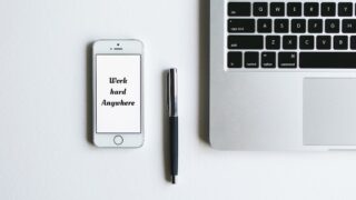 白い机の上に置かれたiPhoneとMacBookのキーボード部分、ペン。Apple製品をイメージした写真