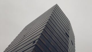 曇り空を背景にした高層ビルの角を見上げた写真