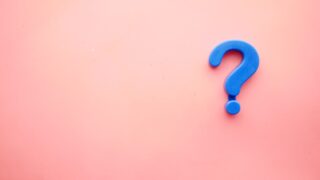 ピンク色の背景に置かれた青いクエスチョンマーク(はてなマーク)のオブジェの写真