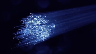 暗闇の中で青白く発光する光ファイバーケーブルの束の写真