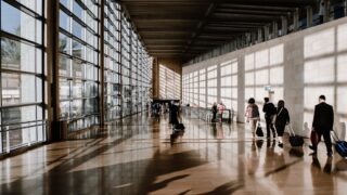 空港の通路をスーツケースを引いて歩く旅行者たちの後ろ姿の写真