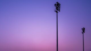 夕暮れの紫〜ピンクの空に浮かぶ2本のナイター照明塔のシルエット。試合開催のイメージ写真