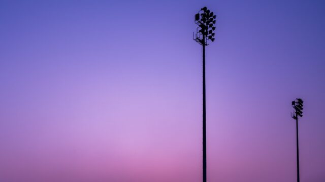 夕暮れの紫〜ピンクの空に浮かぶ2本のナイター照明塔のシルエット。試合開催のイメージ写真