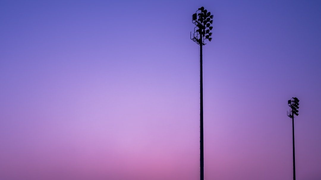夕暮れの紫〜ピンクの空に浮かぶ2本のナイター照明塔のシルエット。試合開催のイメージ写真