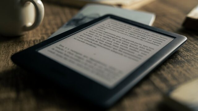木製テーブルの上に置かれた電子書籍リーダー端末。コーヒーカップと本が横に添えられた読書シーン