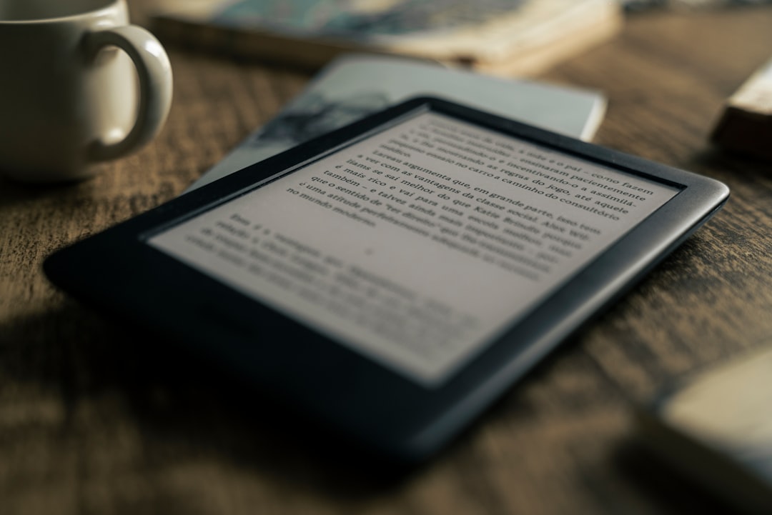 木製テーブルの上に置かれた電子書籍リーダー端末。コーヒーカップと本が横に添えられた読書シーン