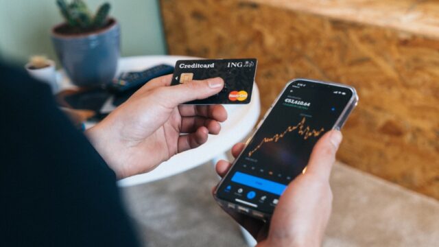 クレジットカードとスマートフォンの資産推移グラフを手に持って確認している写真。月次のポイント実績確認をイメージ。