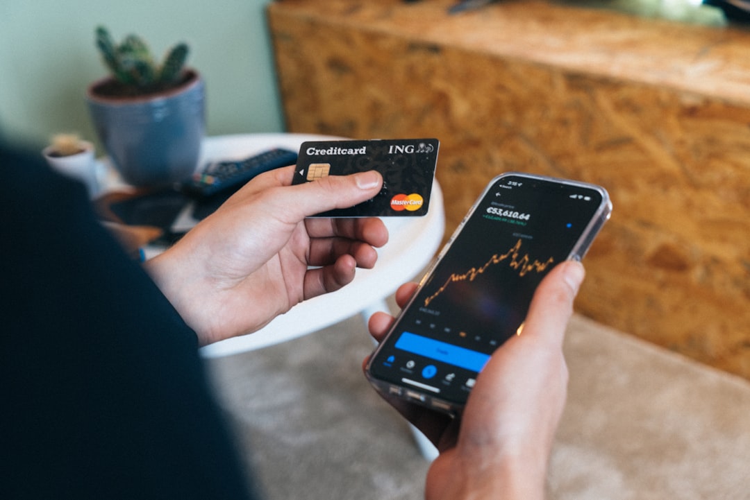 クレジットカードとスマートフォンの資産推移グラフを手に持って確認している写真。月次のポイント実績確認をイメージ。