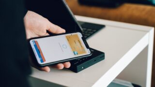 スマートフォンでモバイル決済のカード画面を表示し、カードリーダーにかざしている写真。決済方法の選択をイメージ。