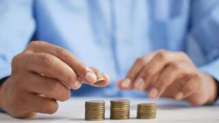 青いシャツを着た人物が硬貨を3つの山に積み上げている写真。SPUのポイント上限まで積み上げるイメージ。