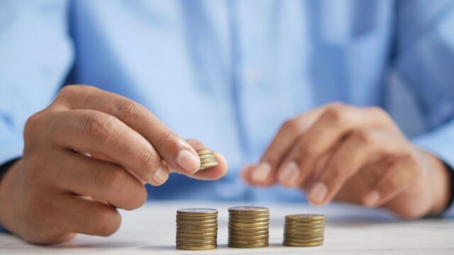 青いシャツを着た人物が硬貨を3つの山に積み上げている写真。SPUのポイント上限まで積み上げるイメージ。