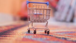 カラフルな織り柄のラグの上に置かれた小さなショッピングカートのミニチュア。複数店舗での買い回りをイメージした写真